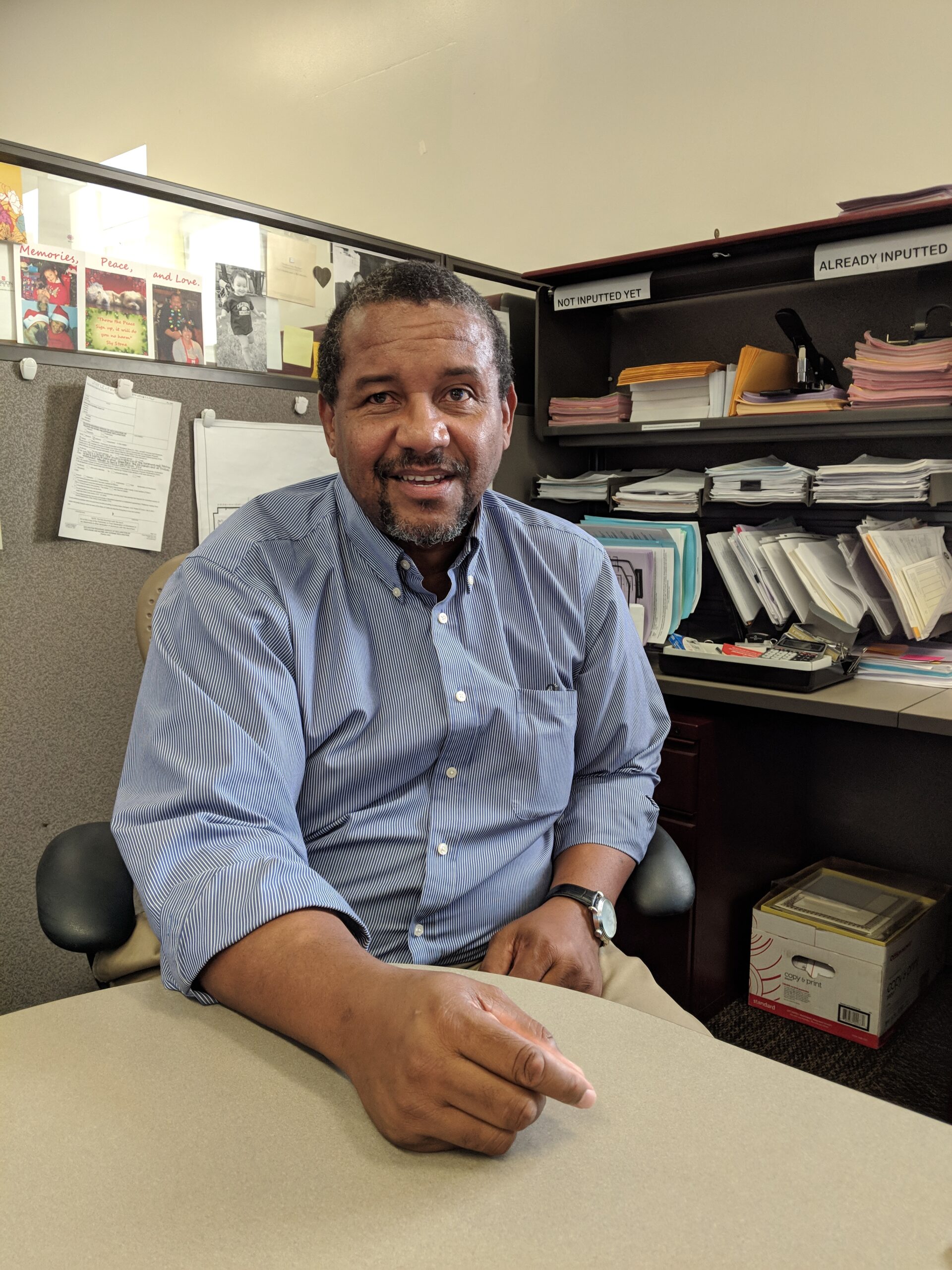 Portrait of Anthony Filer, Directing Attorney sitting at a cubicle desk with paper in the background.